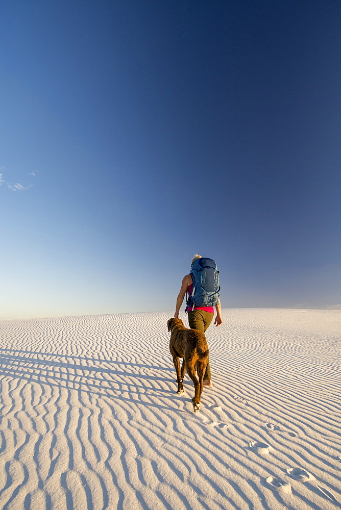 Rear view of female backpacker with dog hiking in desert of White Sands National Monument, Alamogordo, New Mexico, USA