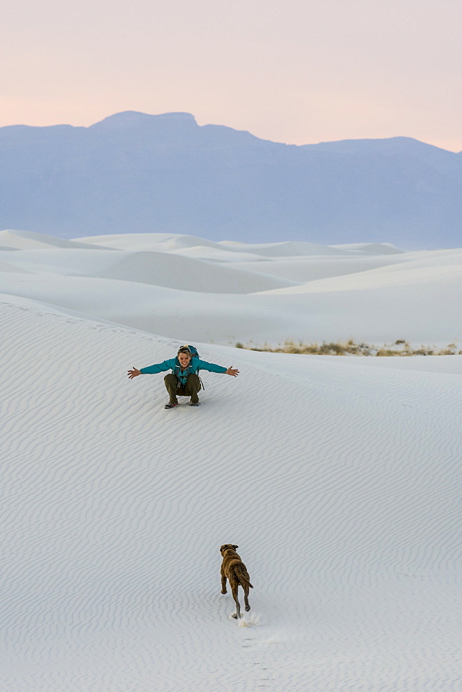 Woman playing with dog while hiking in desert of White Sands National Monument, Alamogordo, New Mexico, USA