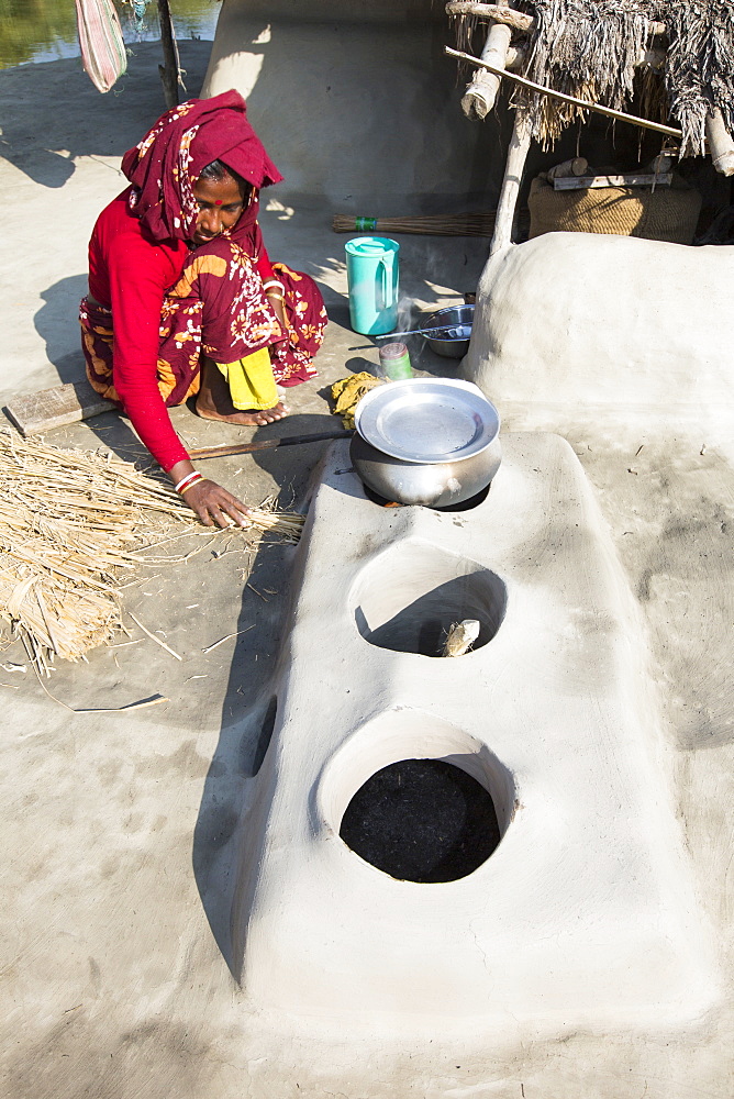 A woman subsistence farmer cooking on a traditional clay oven, using rice stalks as biofuel in the Sundarbans, Ganges, Delta, India. the area is very low lying and vulnerable to sea level rise. All parts of the rice crop are used, and the villagers life is very self sufficient, with a tiny carbon footprint.