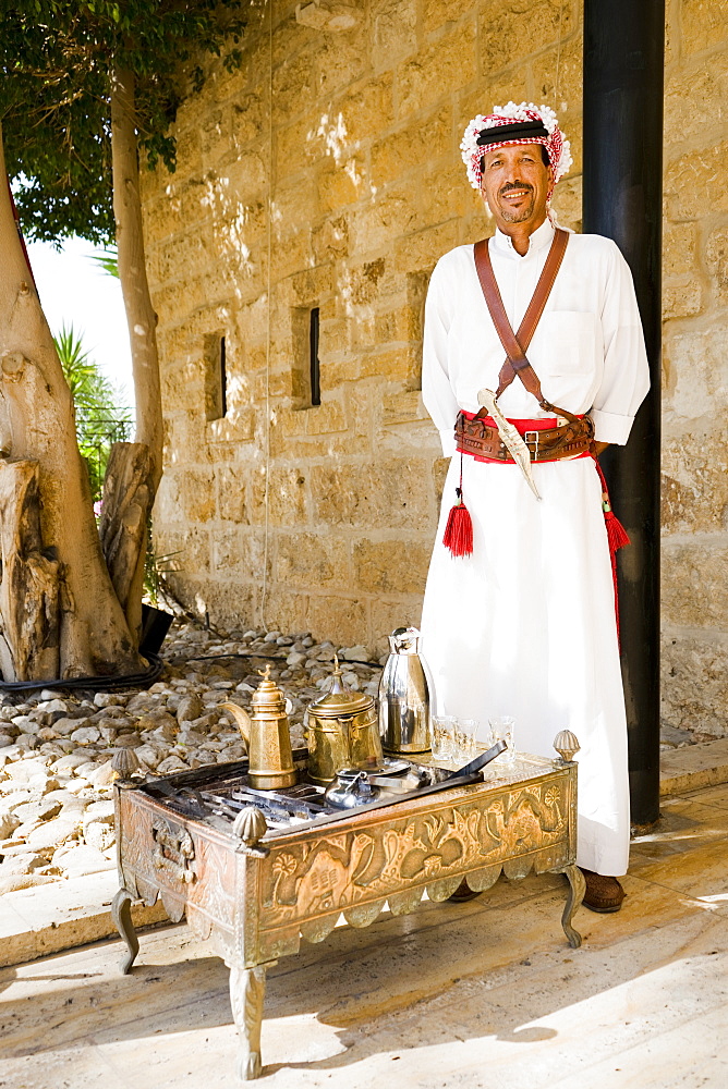 Portrait of man wearing traditional Arabic clothes standing by traditional tea set on engraved tea table, Madaba Governorate, Jordan