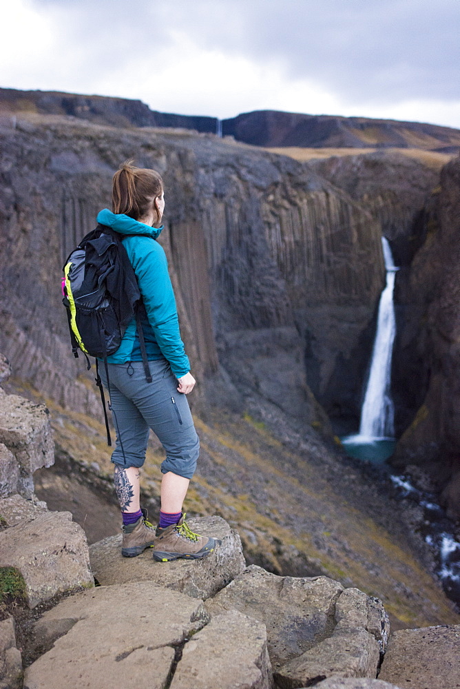 Female backpacker standing on rocks and looking at distant Litlanesfoss waterfall, Iceland