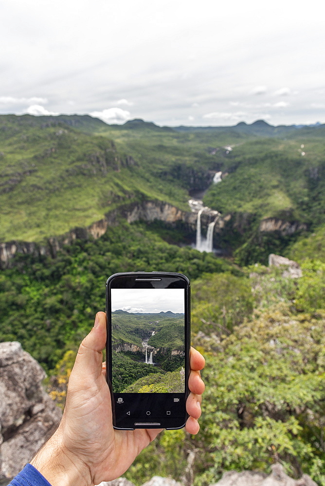 Hand holding mobile phone taking a picture of beautiful cerrado natural landscape with waterfalls in Mirante da Janela, Chapada dos Veadeiros, Goias, central Brazil