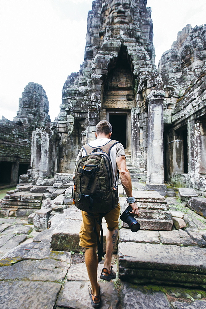 Rear view shot of a single tourist holding a camera exploring ancient Cambodian temple, Siem Reap Province, Cambodia