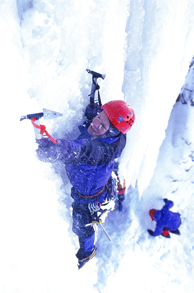 Eric Sast climbing an icy cliff with axes.