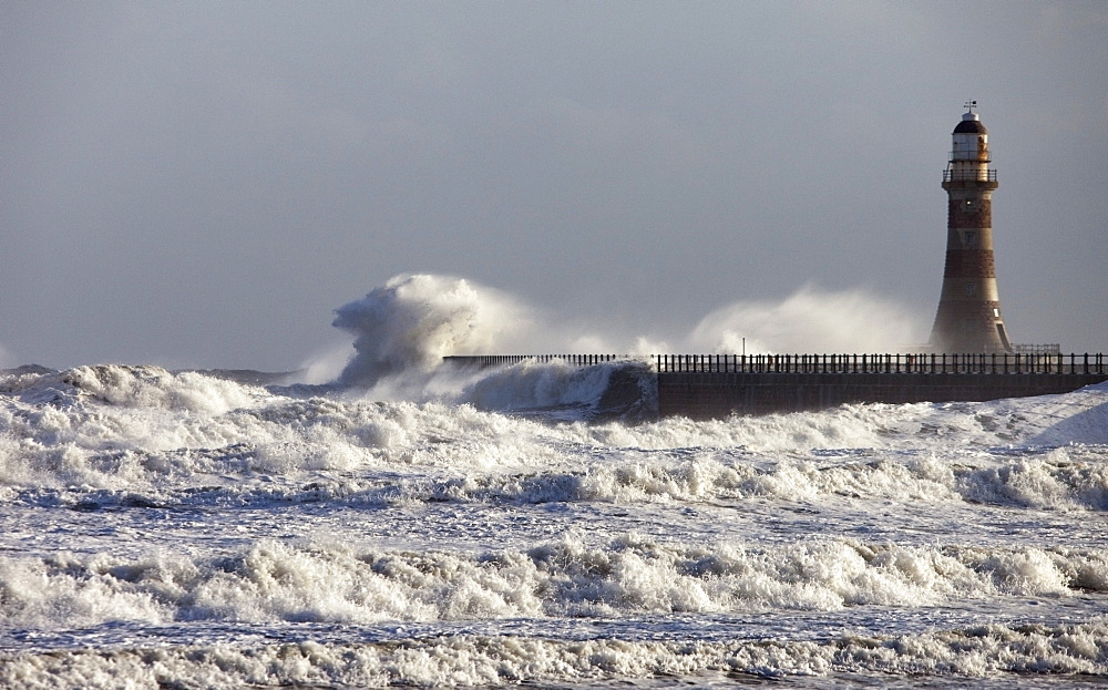 Waves Crashing Against A Pier With A Lighthouse