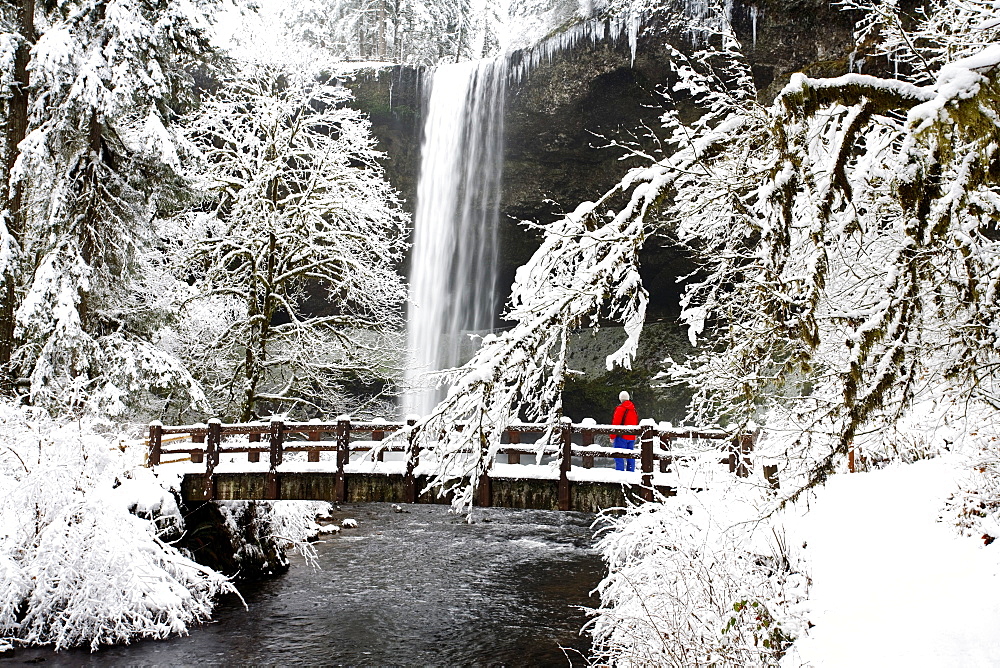 A Person Standing On A Snow Covered Bridge Watching A Waterfall In Winter