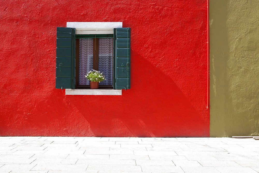 A Flower Pot Sits In A Window With Shutters Open In Building Painted Bright Red, Burano, Venezia, Italy