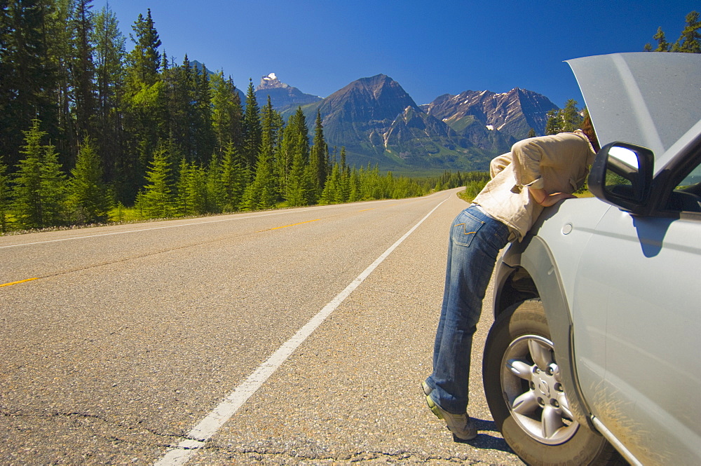 Woman Looking Under Hood Of Her Car On Mountain Road, Alberta Canada