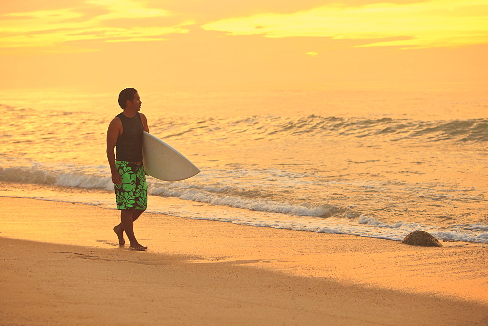 Surfer Walking Down The Beach Along The Water At Sunset, Baja California Sur, Mexico