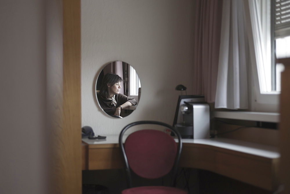 Reflection of a woman in a mirror as she looks out the window