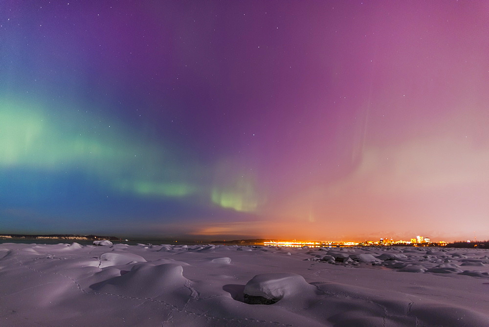 Northern lights shine above city skyline in this nighttime view from the tony knowles coastal trail in winter, Anchorage alaska united states of america