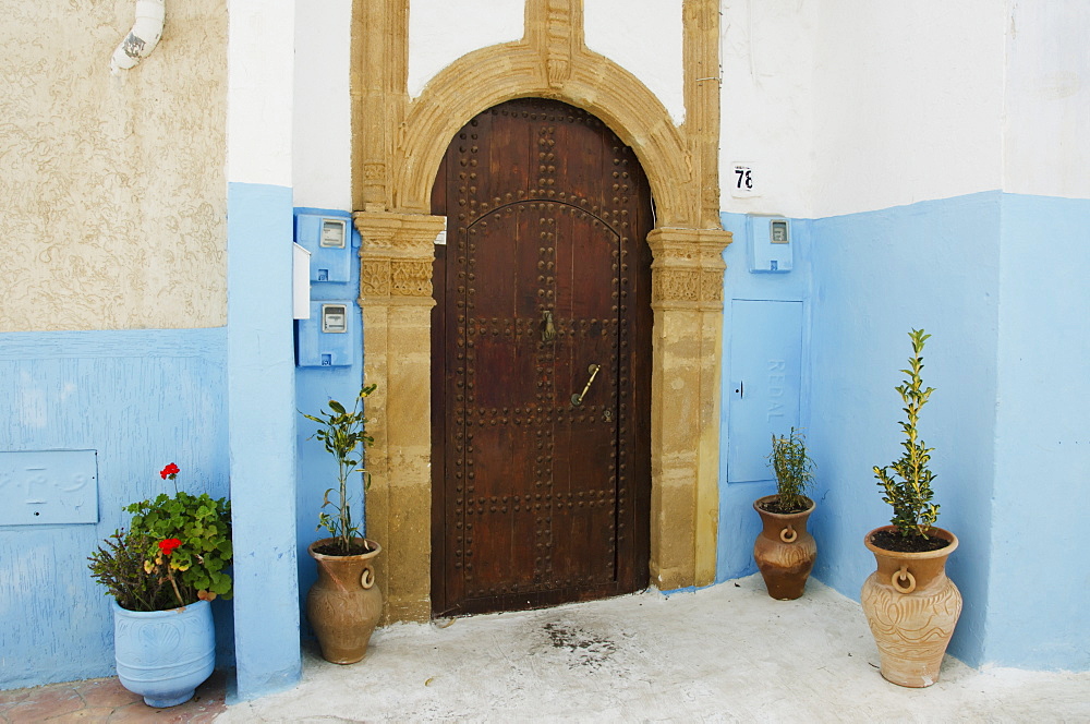 A house with an arched wooden door with rivets and painted blue walls in old town, Rabat morocco