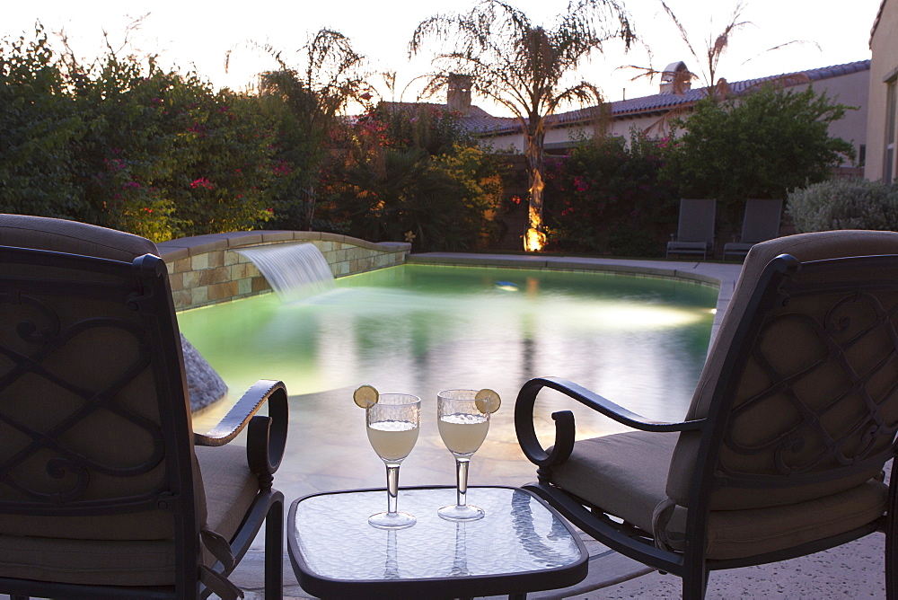 Pool Side Setting At Dusk With Pool Lights Two Chairs Table And Two Glasses With Lime Wedges, Palm Springs, California, United States of America