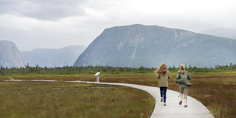 Two Young Women Walking On A Wooden Boardwalk At Norris Point, Newfoundland And Labrador, Canada