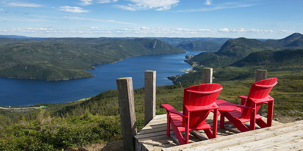 Two Red Adirondack Chairs On A Wooden Deck Overlooking Bonne Bay, Newfoundland And Labrador, Canada