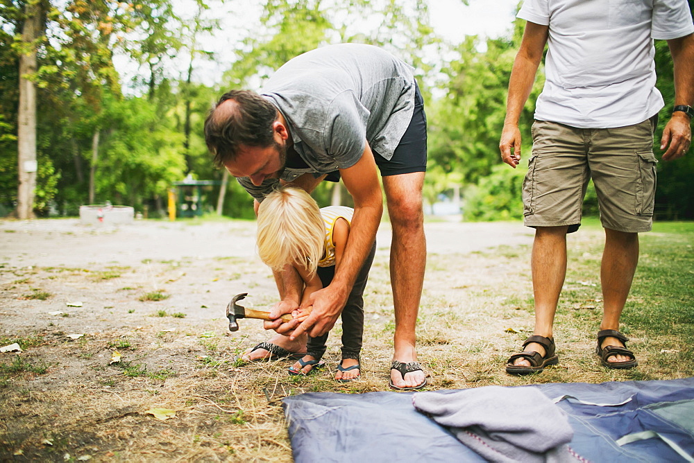 A Father And Young Daughter Work Together To Hammer In Tent Pegs At A Campsite, Peachland, British Columbia, Canada