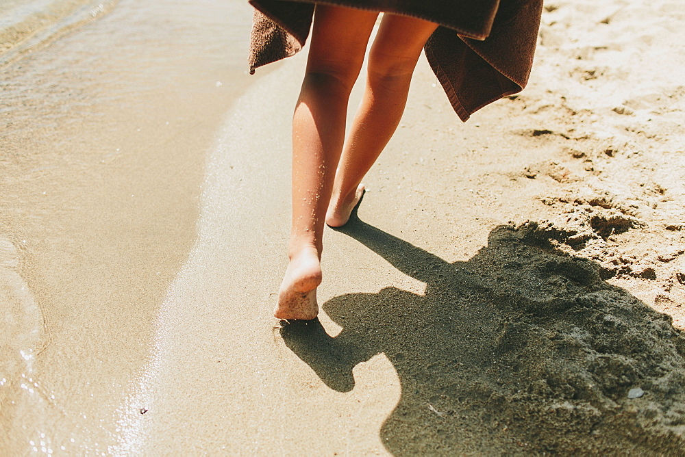 A Girl Walks Barefoot In The Sand Along The Water's Edge, Peachland, British Columbia, Canada