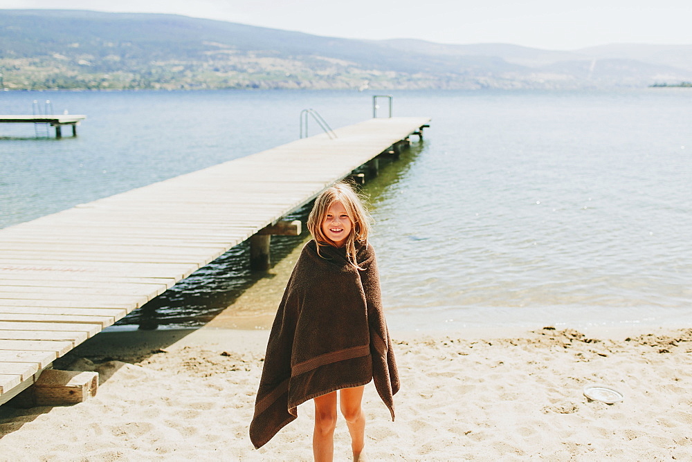 A Girl Stands On The Beach At The Edge Of Lake Okanagan, Peachland, British Columbia, Canada