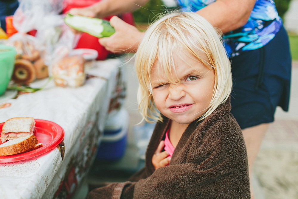 A Young Girl Winking At The Camera As She Sits At A Picnic Table For A Meal, Peachland, British Columbia, Canada