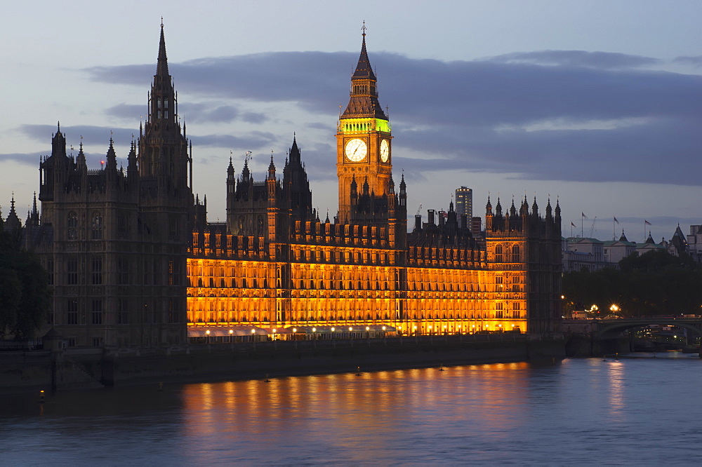 A Building And Clock Tower Along The Water's Edge Illuminated At Dusk, London, England