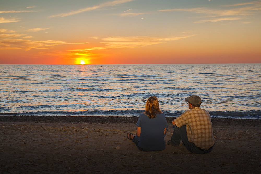 A Man And Woman Sit On A Beach Watching The Sunset On Lake Erie, Presque Isle State Park, Erie, Pennsylvania, United States Of America