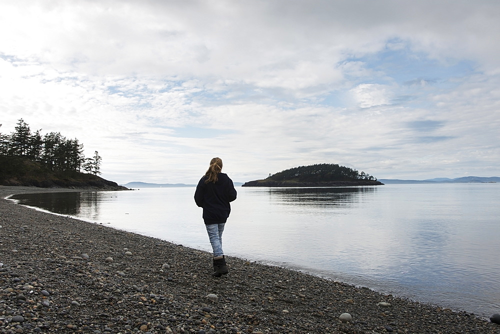 A Young Woman Walks On A Rocky Beach In Deception Pass State Park, Oak Harbor, Washington, United States Of America