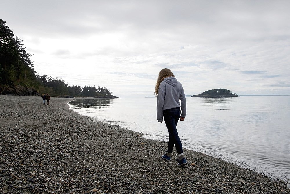 A Young Woman Walks On A Rocky Beach In Deception Pass State Park, Oak Harbor, Washington, United States Of America