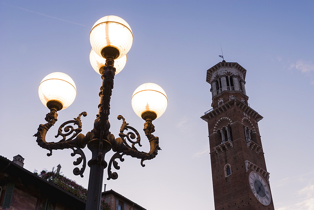 A Clock Tower And Illuminated Lamp Post In Piazza Delle Erbe At Dusk, Verona, Italy