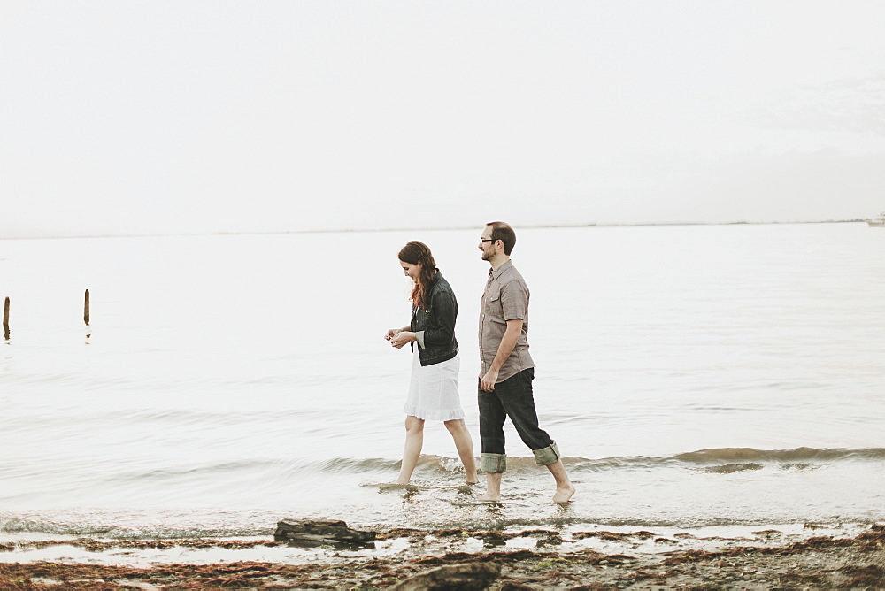 A Couple Walking Barefoot Along The Water's Edge, Crescent Beach, British Columbia, Canada