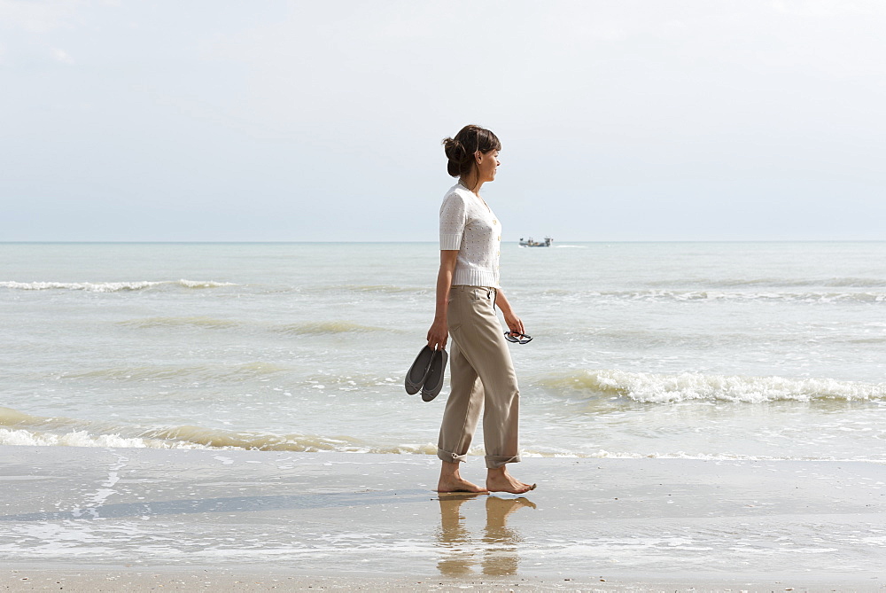 A Woman Walking On The Wet Beach Carrying Her Shoes, Rimini, Emilia-Romagna, Italy