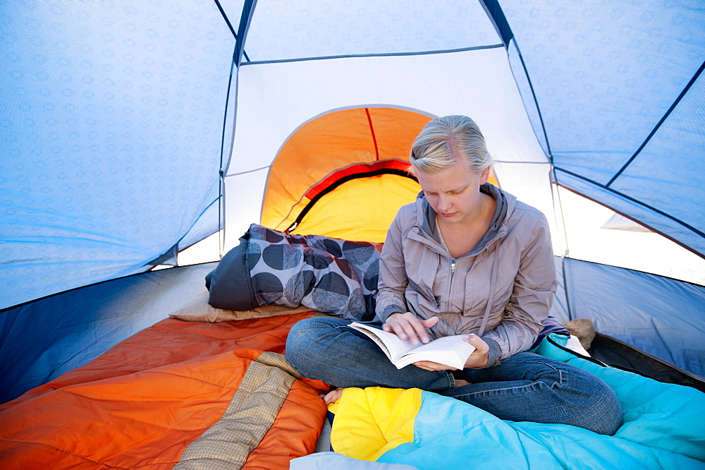 A Young Woman Reading A Book Inside A Tent, California, United States Of America