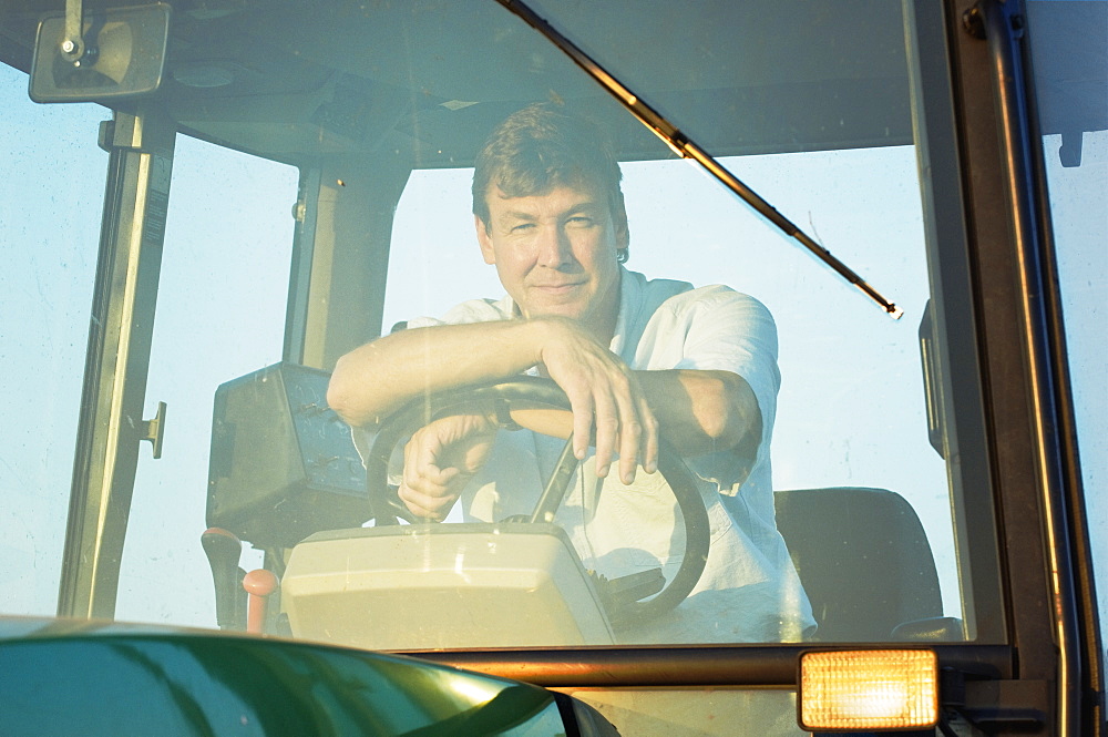 Agriculture - A farmer sitting in the cab of his John Deere tractor in late afternoon sunlight / near Hoffman, Minnesota, USA.