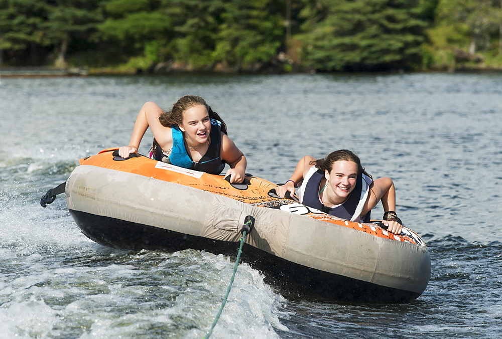 Two Teenage Girls Riding In An Inner Tube Being Pulled By A Boat On A Lake, Ontario, Canada