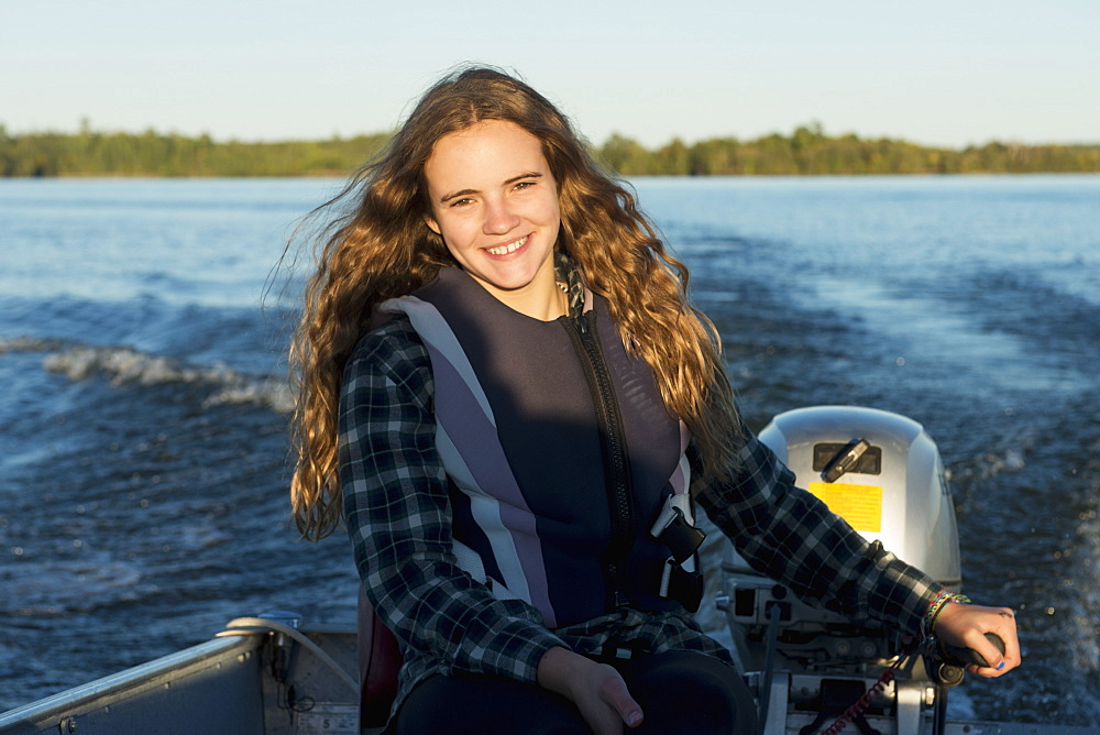 A Teenage Girl Sits By The Motor At The Back Of A Motorboat With Her Face Illuminated By Sunlight, Ontario, Canada