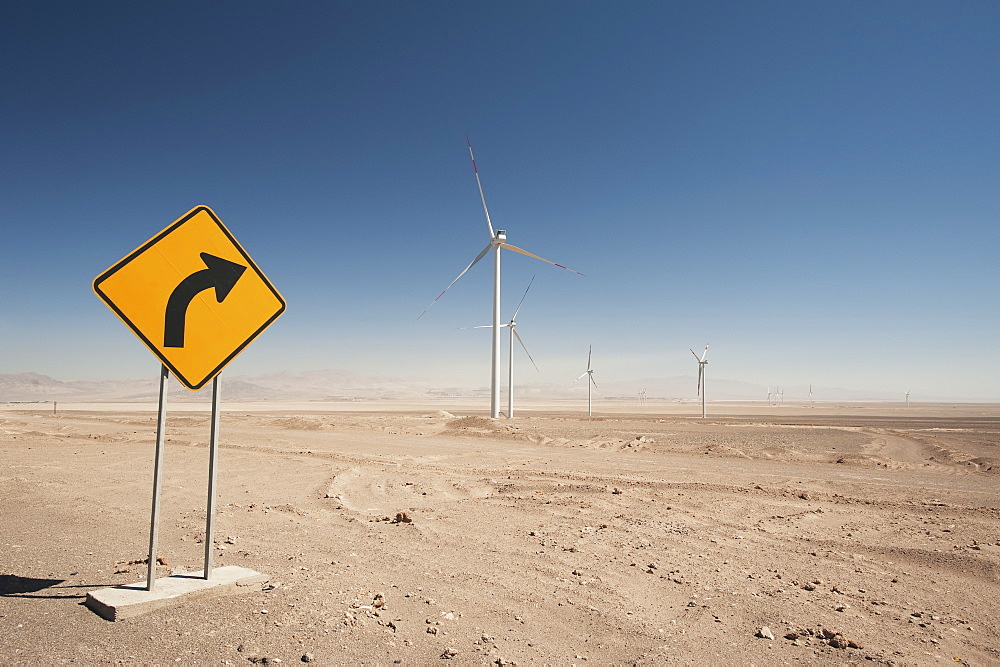 Wind Turbines In The Atacama Desert With A Yellow Sign Indicating A Curve, Calama, Chile