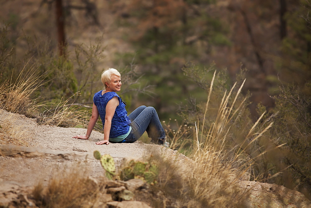 Portrait Of A Woman Sitting On A Large Rock, Leaning Back On Her Hands, With Her Head Turned And Smiling, United States Of America