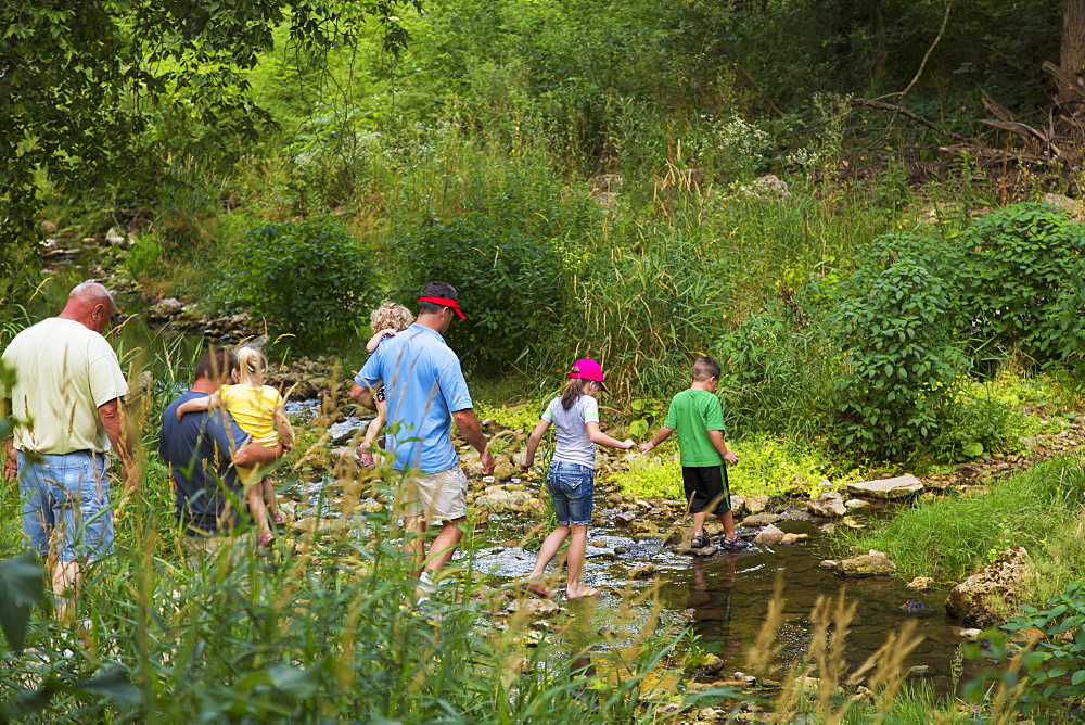 Family Crossing Bear Creek On Hiking Trail Leading To The Ice Cave At Bixby State Preserve, Near Edgewood, Iowa, United States Of America