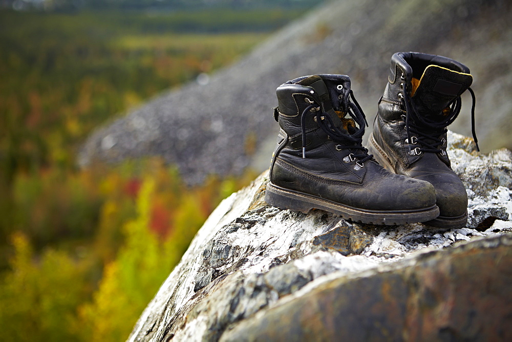 Work Boots On A Rock With Autumn Coloured Trees In The Background, Quebec, Canada