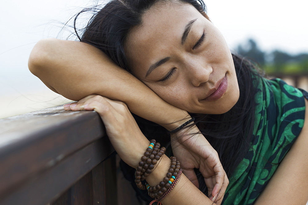 A Young Woman Lays Her Head Against A Wooden Railing At The Beach, Jincheng, Kinmen, Taiwan