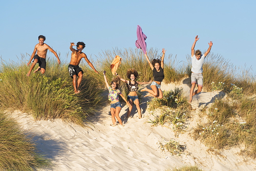 A Group Of Teenagers Running And Jumping Over Sand And Beach Grass, Tarifa, Cadiz, Andalusia, Spain