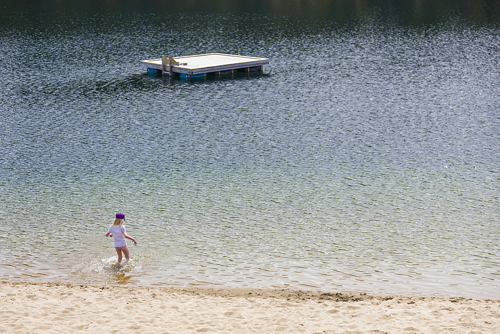 A Young Girl Plays In The Water Along A Sandy Beach, Lucky Lake, Yukon Territory, Canada, Summer