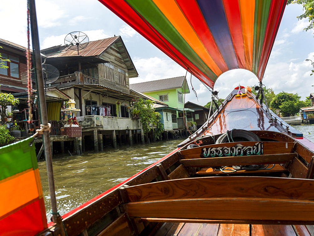 A Boat On The River With A Colourful Cover And Houses Along The Shoreline, Bangkok, Thailand