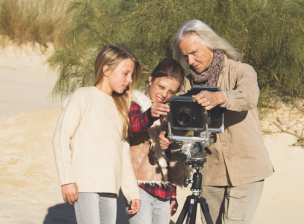 A Female Photographer Shows Two Young Girls Images On A Camera With Tripod On The Beach, Tarifa, Cadiz, Andalusia, Spain