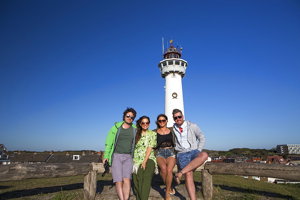 A Group Of Friends Standing With A Lighthouse In The Background Outside Of Amsterdam Central, Egmond Aan Zee, Holland