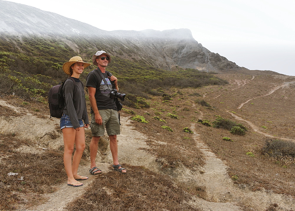 A Young Couple Stands On A Rugged Dirt Trail On A Mountainous Landscape Looking Out, Praia Da Cordoama, Portugal