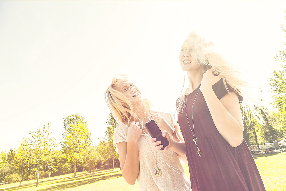 Two Sisters Having Fun Outdoors And Singing Together In A City Park While Listening To Music On An Mp-3 Player, Edmonton, Alberta, Canada