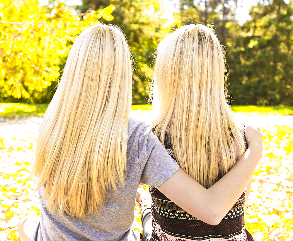 View From Behind Of Two Sisters Hanging Out In A City Park Together In Autumn, Edmonton, Alberta, Canada