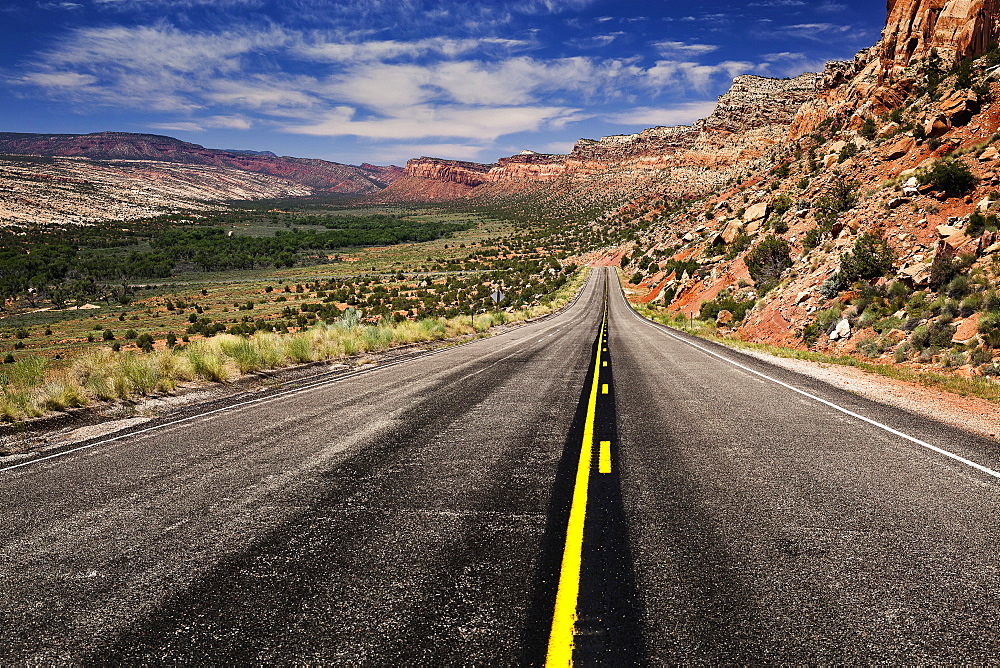 Utah Highway Stretching Into The Distance With Rock Cliffs Wrapping From The Right Side Foreground Around To The Background Center And Left Of The Photo With Blue Skies With Some Clouds, Utah, United States Of America