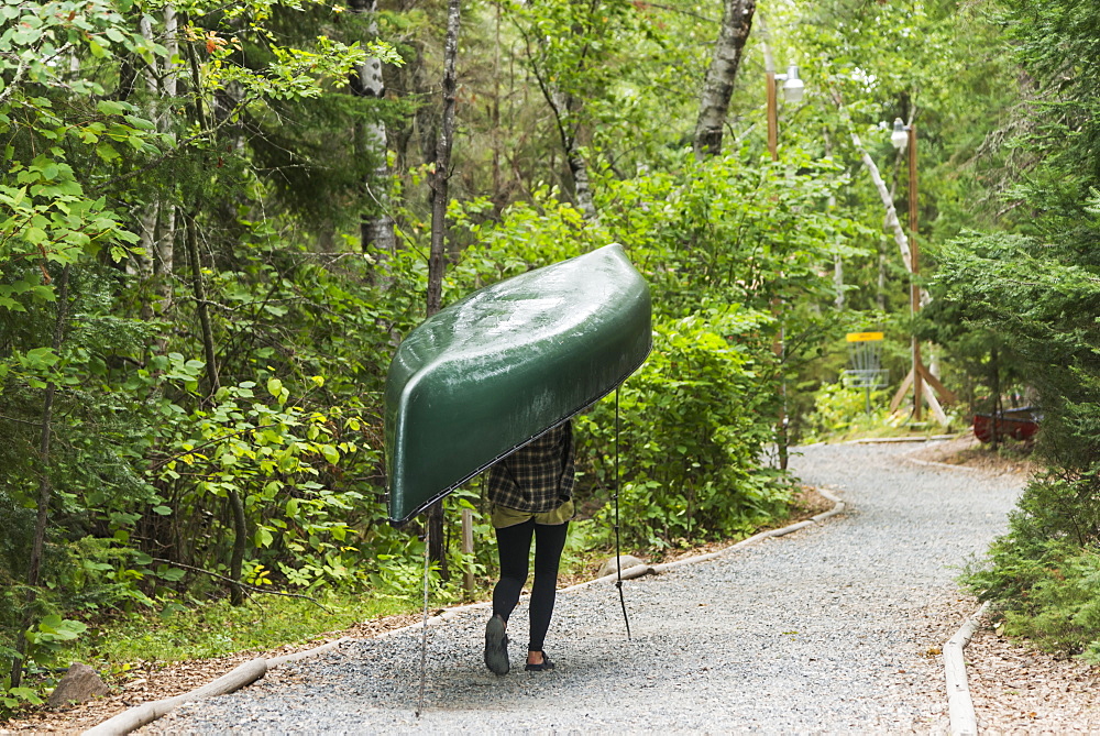 A Young Woman Carrying A Green Canoe On Her Head Down A Trail, Ontario, Canada