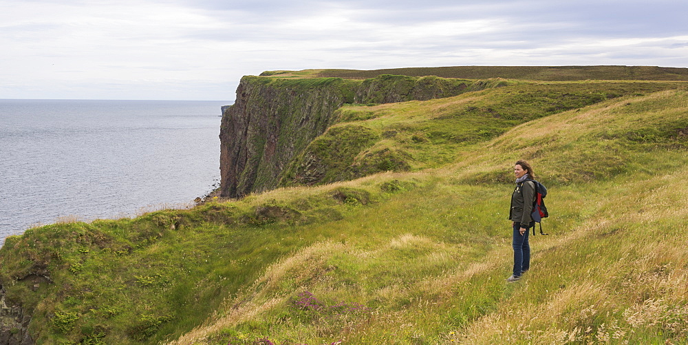 A Woman Stands On Grass Near A Ridge Overlooking Duncansby Head, John O'groats, Scotland